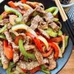 Healthy black pepper beef stir fry with tender beef strips and red and green bell peppers in a skillet