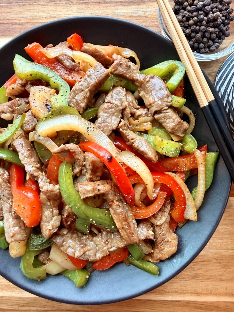 Healthy black pepper beef stir fry with tender beef strips and red and green bell peppers in a skillet