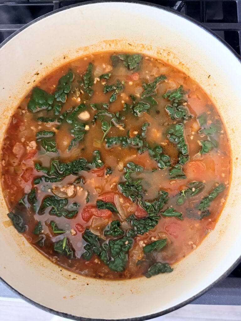 Chopped lacinato kale wilting into tomato sausage and white bean soup.