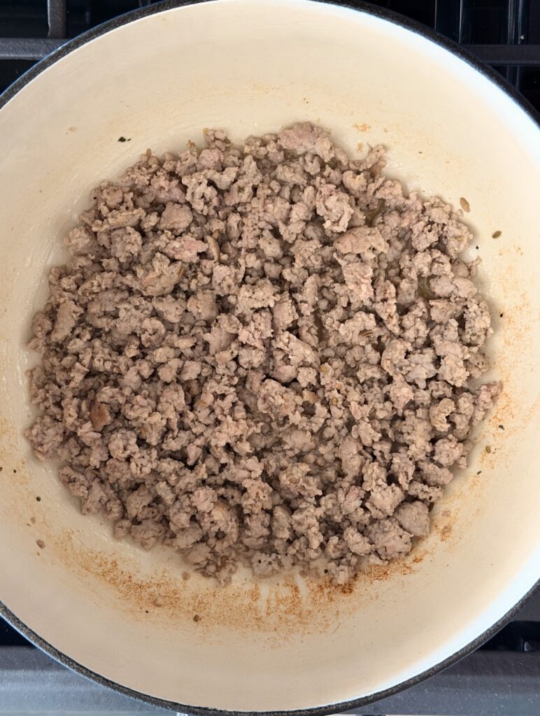 Crumbled Italian sausage cooking in a white Dutch oven for creamy gnocchi soup.