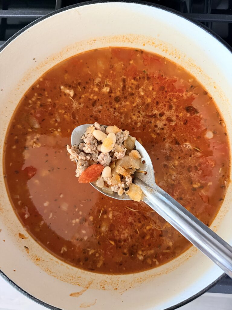 Spoonful of sausage, cannellini beans, and tomatoes lifted from simmering tomato broth.