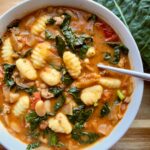 Creamy Tuscan sausage kale soup with cannellini beans and basil served over gnocchi in a bowl