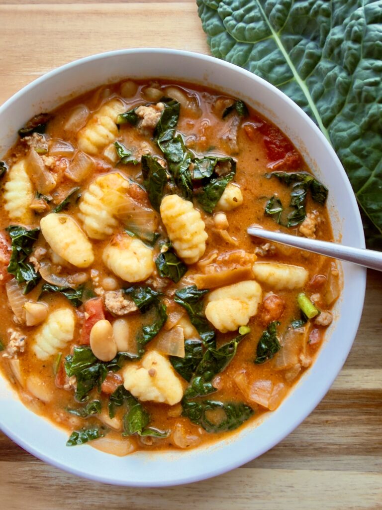 Creamy Tuscan sausage kale soup with cannellini beans and basil served over gnocchi in a bowl