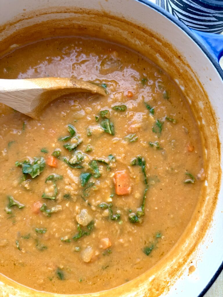 Creamy red lentil soup with kale and lemon in a bowl, finished with cilantro and olive oil