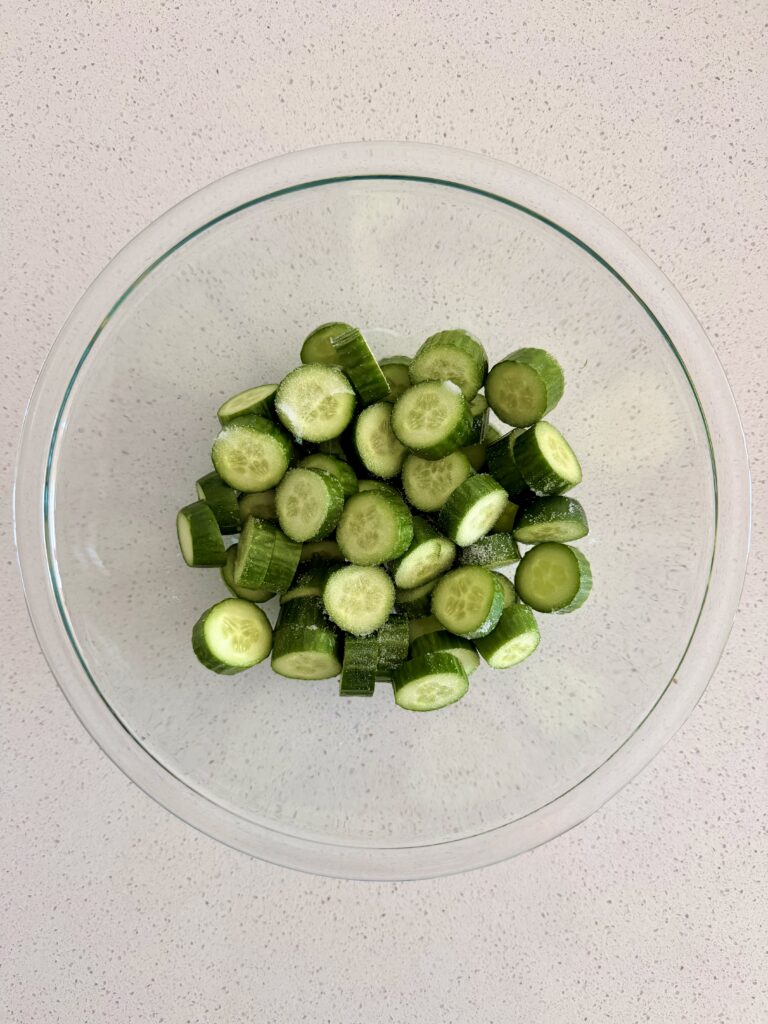 Sliced Persian cucumbers sprinkled with salt in a glass bowl for Korean cucumber salad (oi muchim)