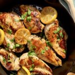 Golden lemon garlic chicken cutlets cooking in a cast iron skillet with fresh lemon zest and herbs