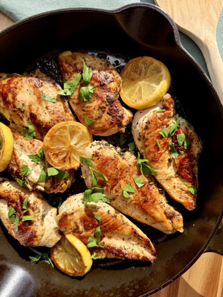 Golden lemon garlic chicken cutlets cooking in a cast iron skillet with fresh lemon zest and herbs