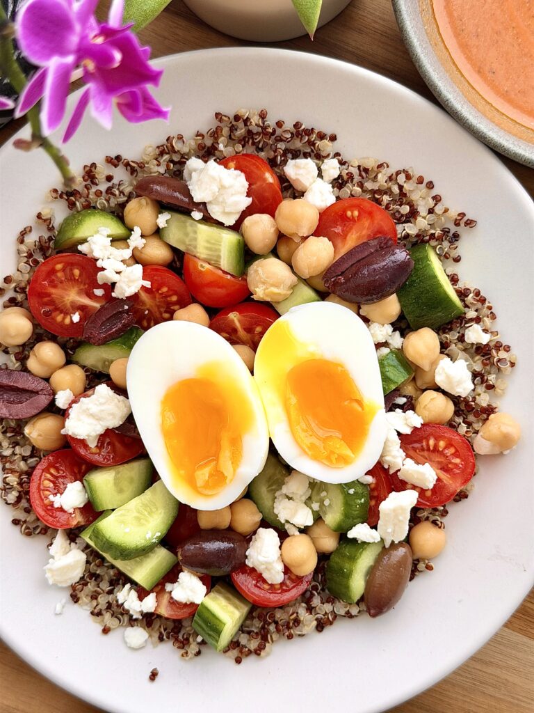 high-protein Mediterranean quinoa breakfast bowl with egg, chickpeas, feta, vegetables, olives, and tahini harissa dressing