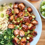 Cubed salmon teriyaki served in a bowl with rice, vegetables, scallions, and sesame seeds