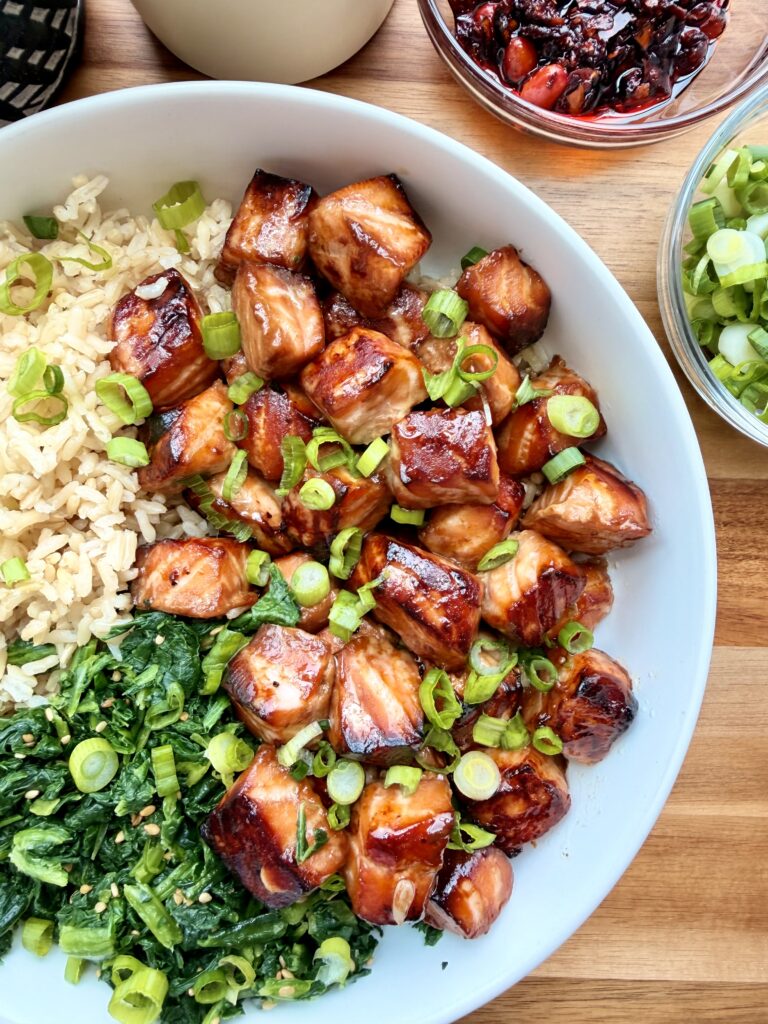 Cubed salmon teriyaki served in a bowl with rice, vegetables, scallions, and sesame seeds