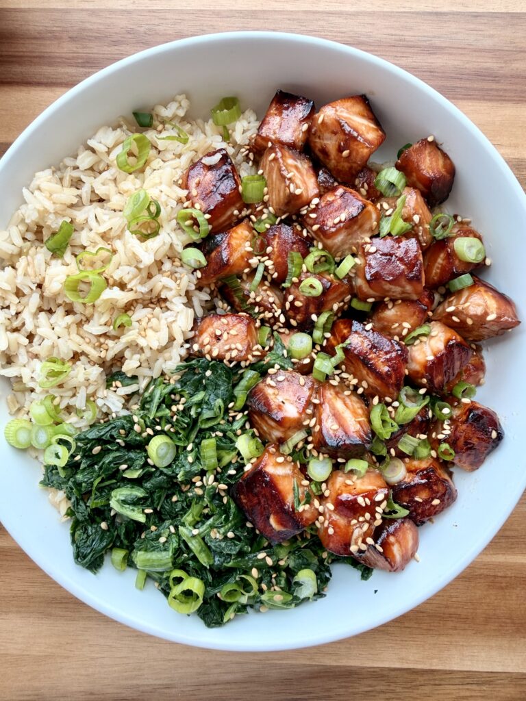 Cubed salmon teriyaki layered over a whole grain with vegetables, finished with scallions and sesame seeds