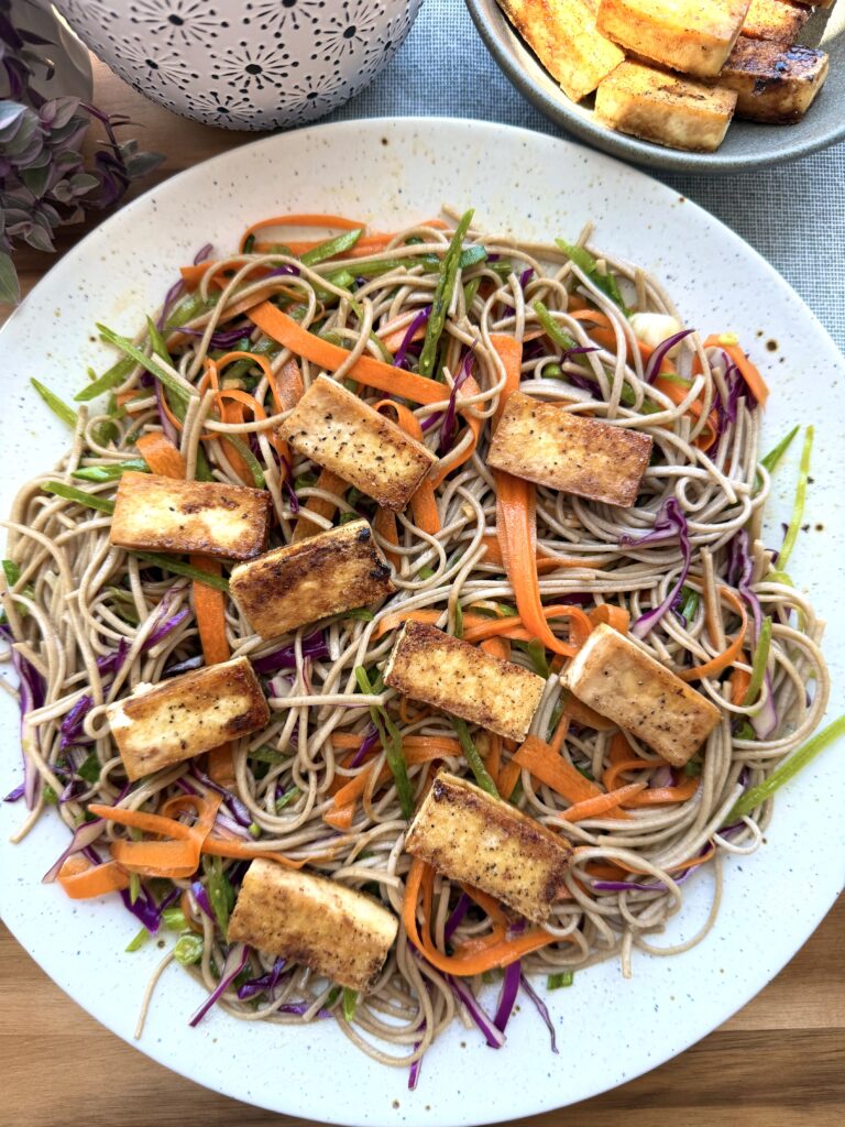 High-protein soba noodle salad with crispy tofu, red cabbage, snow peas, carrots, edamame, sesame dressing, and chili crisp.