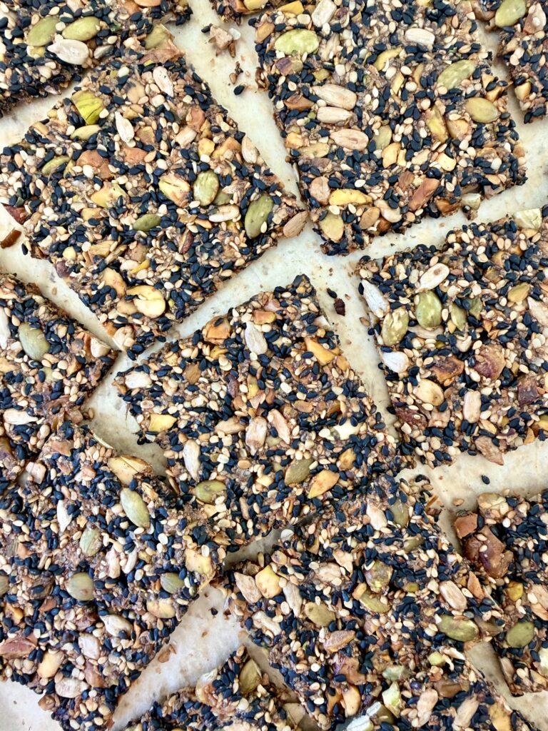 Close-up of crisp black sesame seed crackers with pistachios, pumpkin seeds, and sunflower seeds on parchment paper.