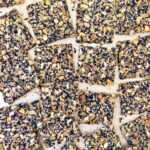 Overhead view of black sesame seed crackers cut into squares, showing pistachios, pumpkin seeds, and sunflower seeds.