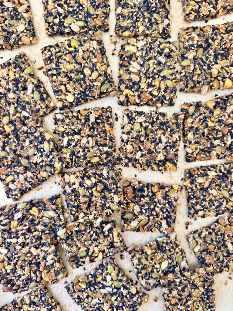 Overhead view of black sesame seed crackers cut into squares, showing pistachios, pumpkin seeds, and sunflower seeds.