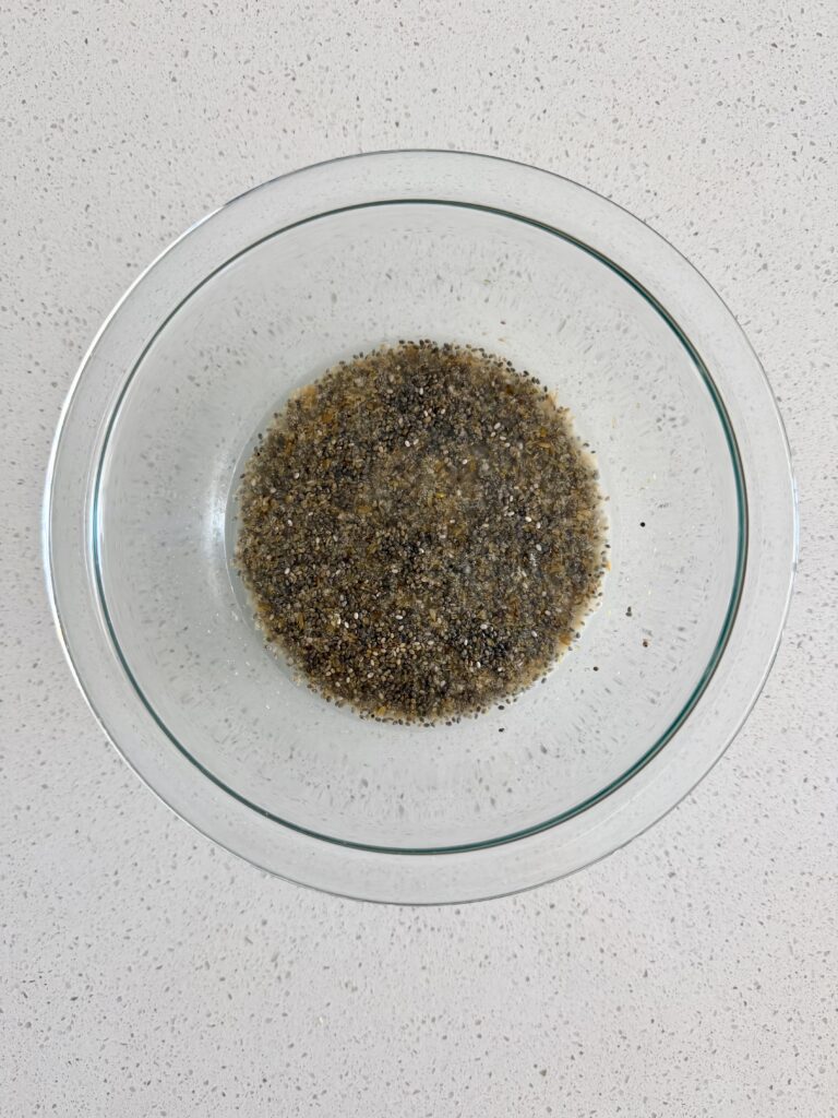Ground flaxseed and chia seeds soaking in water in a glass bowl to form a binder for seed crackers.