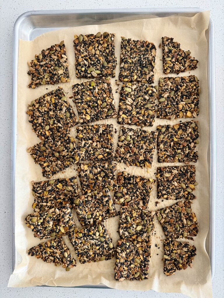 Baked black sesame seed crackers cooled and broken into squares along the scored lines on a parchment-lined baking sheet.