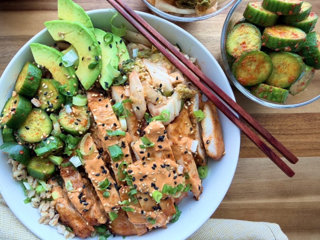 Gochujang Chicken Bowls with creamy gochujang yogurt sauce, kimchi, avocado, cucumber salad, scallions, sesame seeds, and farro.