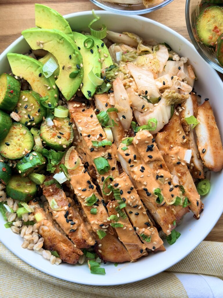 Gochujang Chicken Bowls with creamy gochujang yogurt sauce, kimchi, avocado, cucumber salad, scallions, sesame seeds, and farro.