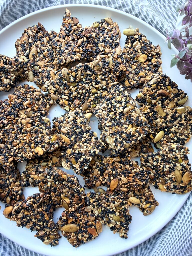 Healthy Black Sesame Seed Crackers arranged on a white platter, made with black sesame seeds, white sesame seeds, pistachios, pumpkin seeds, sunflower seeds, hemp hearts, flaxseed, and chia seeds.