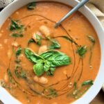 Bowl of creamy roasted tomato white bean soup with spinach, cannellini beans, fresh basil, and a swirl of olive oil