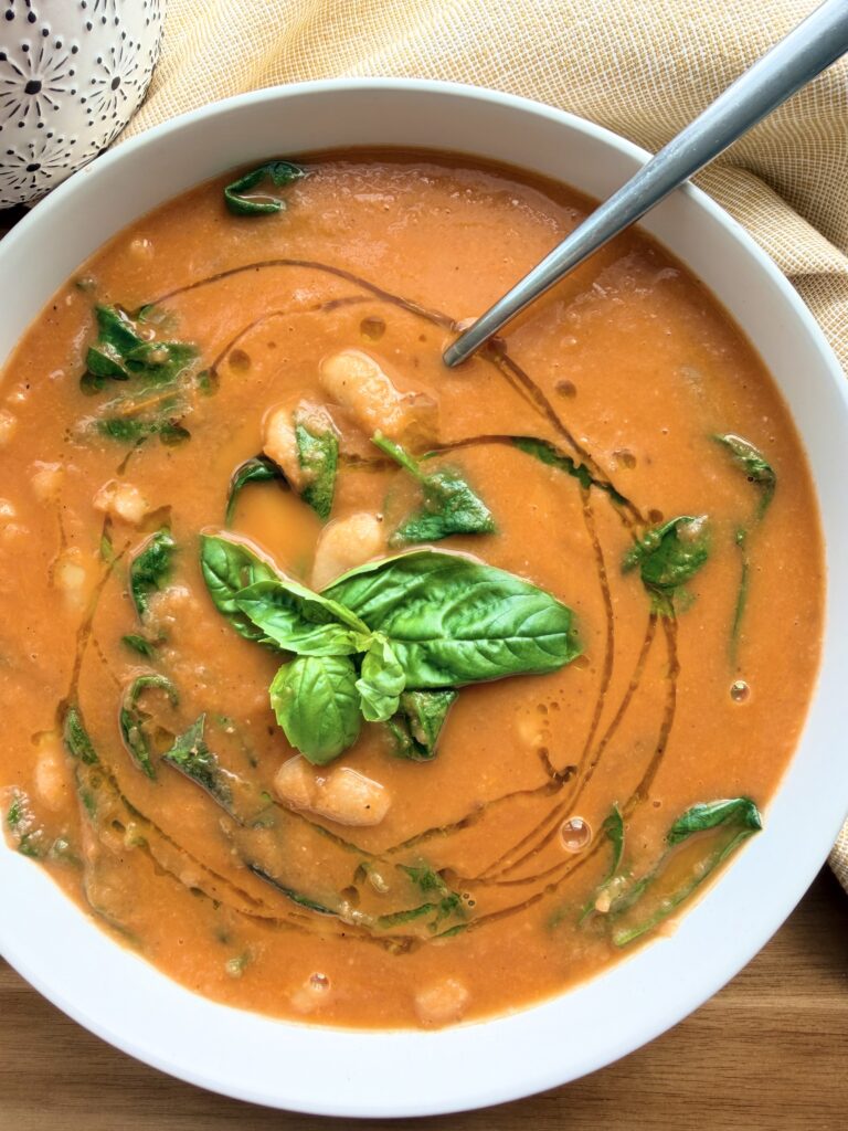 Bowl of creamy roasted tomato white bean soup with spinach, cannellini beans, fresh basil, and a swirl of olive oil