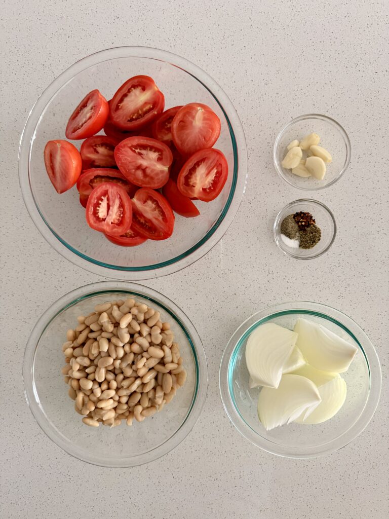 Prepped ingredients for roasted tomato white bean soup: plum tomatoes, onion, garlic, cannellini beans, and spices