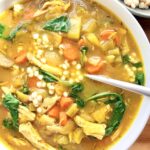 Close-up of golden ginger turmeric chicken soup with pearl couscous, shredded chicken, carrots, celery, and baby spinach