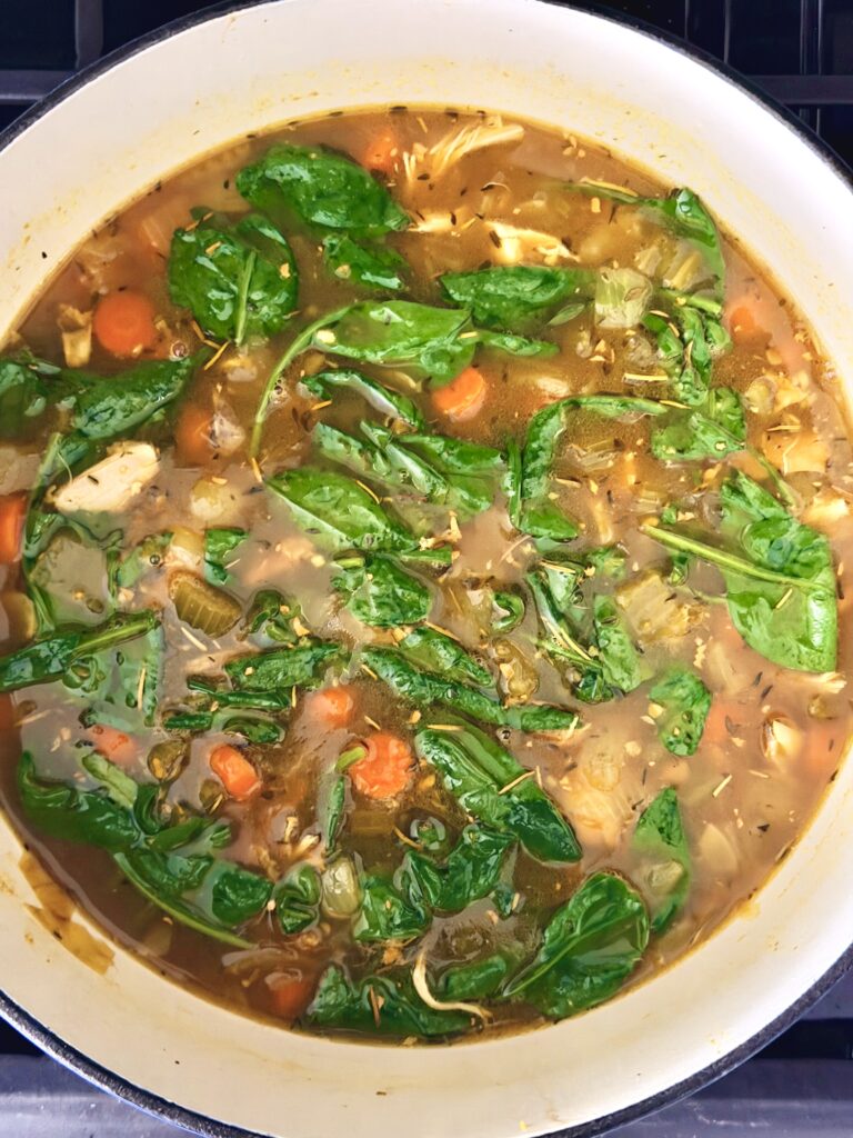 Shredded chicken and baby spinach added to ginger turmeric chicken soup in a Dutch oven
