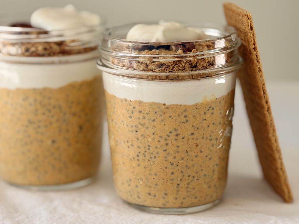Two jars of pumpkin cheesecake chia pudding layered with Greek yogurt and graham cracker crumble, with a graham cracker leaning against the jar