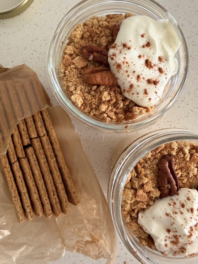 Overhead view of pumpkin cheesecake chia pudding jars topped with crushed graham crackers, pecans, and Greek yogurt dusted with cinnamon powder